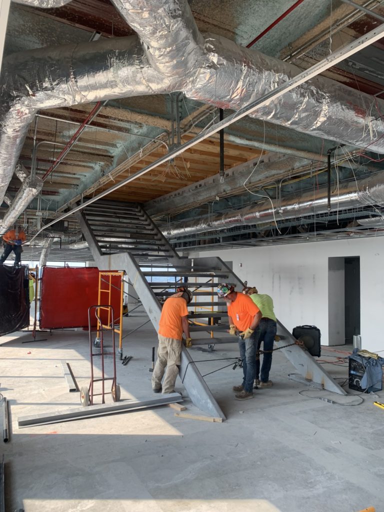 workers in hard hats and bright shirts install a metal and concrete stairway at an indoor construction site